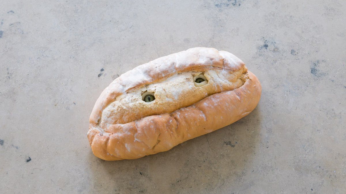 A cast of a loaf of bread with small eyes on it, whilst made out of ceramic it looks like a real piece of bread.