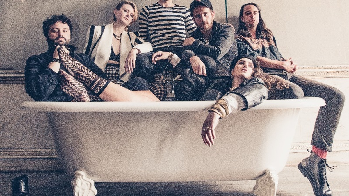 A group of people sit in a bathtub, fully clothed.