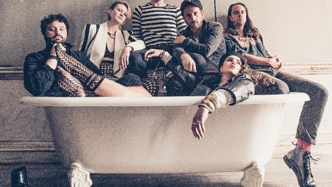 A group of people sit in a bathtub, fully clothed.