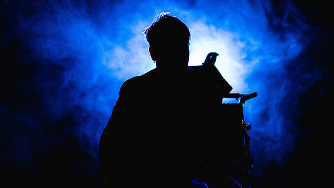 A shadowed figure of woman in a wheel chair with a bright light shining behind her.