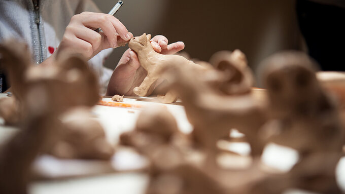 A close up of someone creating a figurine of a cat out of clay.