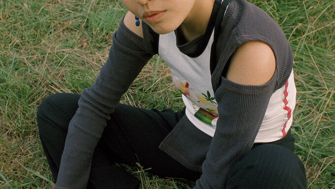 April Lin a non binary East Asian person with green dyed hair, wearing streetwear and are crouched on a grassy field