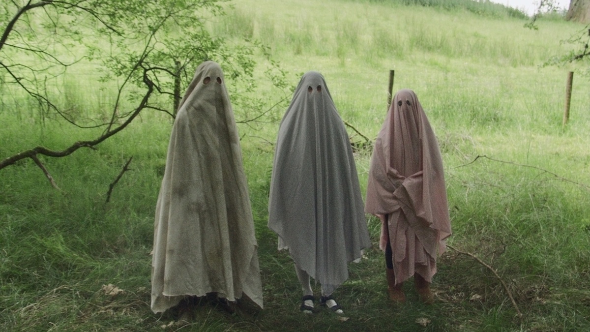 Three people dressed in homemade ghosts outfits, stand in a line, ominiously in the woods.