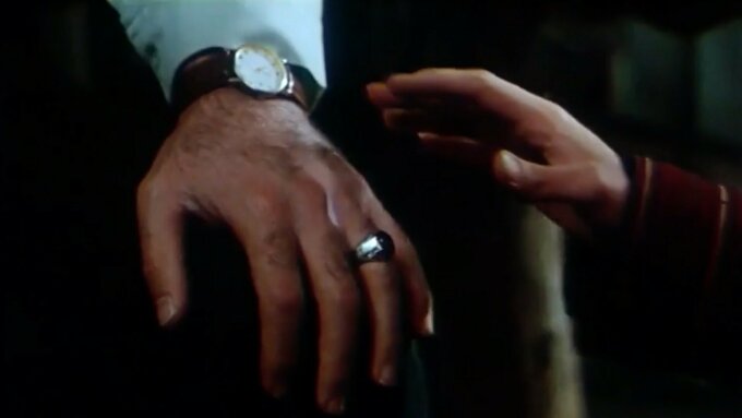 Film still of a hand tenderly brushing another hand wearing a wedding ring.