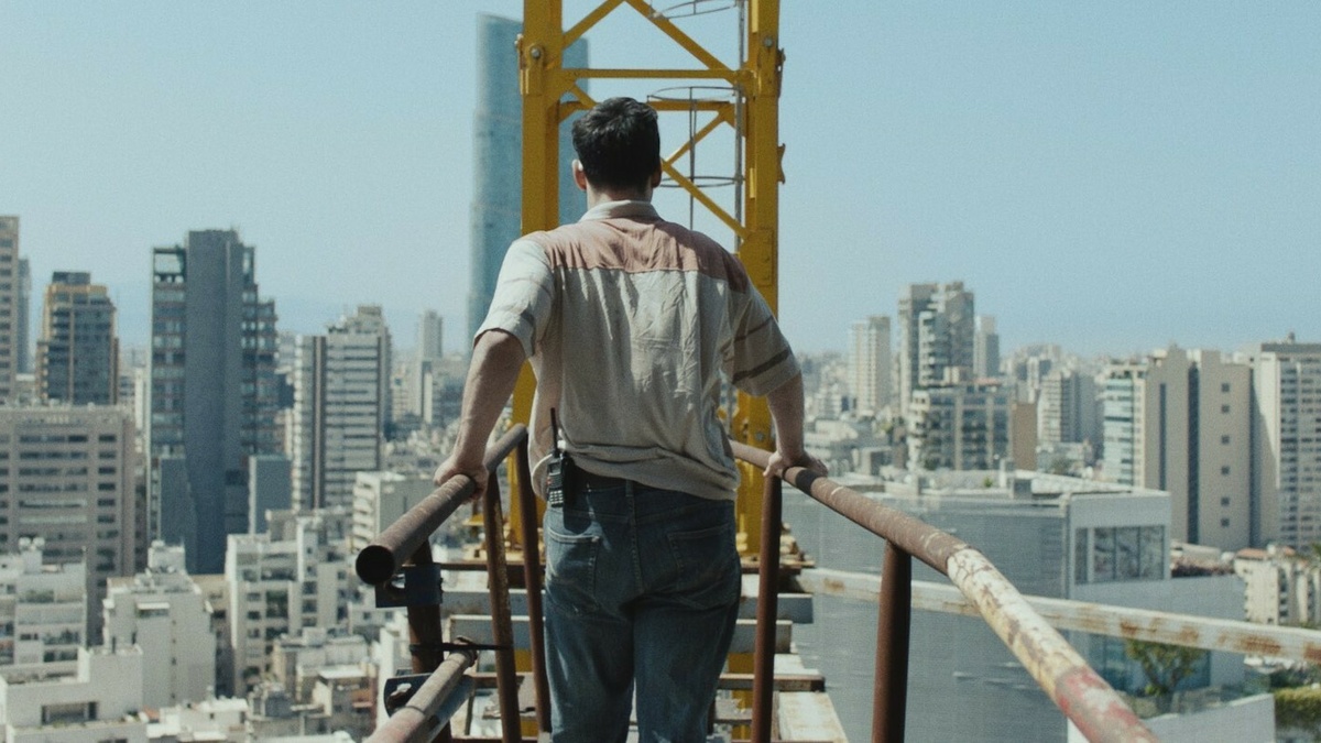 Man walking on high structure to reach crane. Large city skyline in the background.