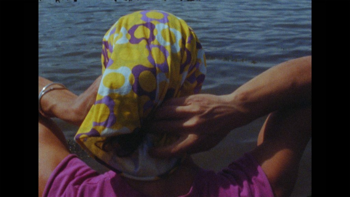 A person is overlooking the ocean wearing a headscarf made up of yellow, blue and purple patterns.