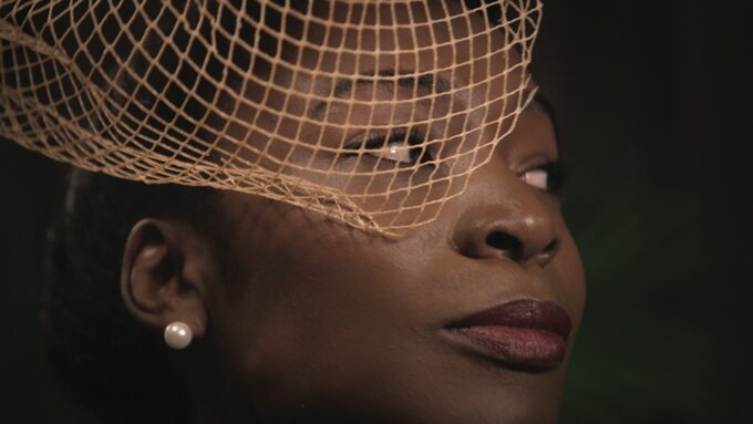 A close-up of Angelica Ross as Georgia, a black trans women wearing light make-up, pearl earrings and a fascinator.