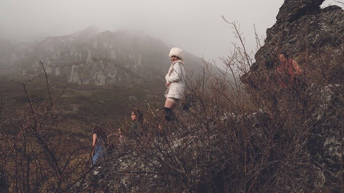 Spanish mountains with 5 trans characters in shot. Centred, Alicia de Benito stands in a white outfit & black boots.