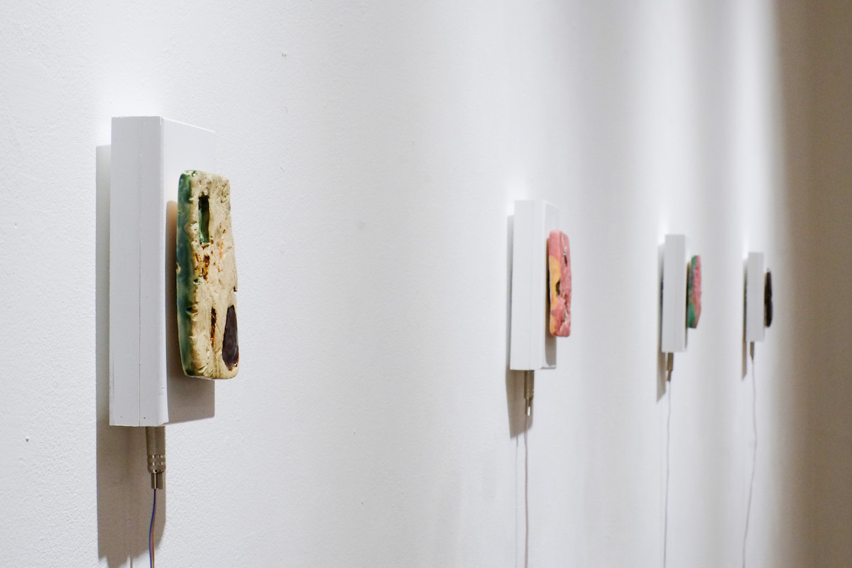 4 multi-coloured clay sound sculptures mounted to the wall on white blocks with a wire coming out the bottom.