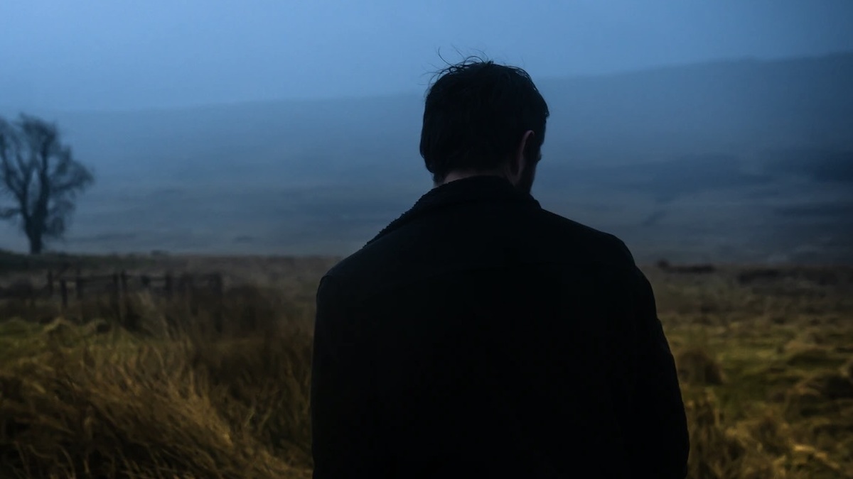 A man is seen in silhouette against a dark Highland landscape.