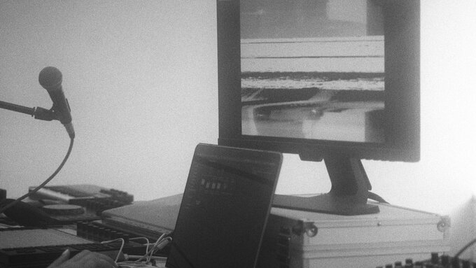 A black and white photo of a microphone and laptop sat in front of a computer screen displaying distorted glitchy images