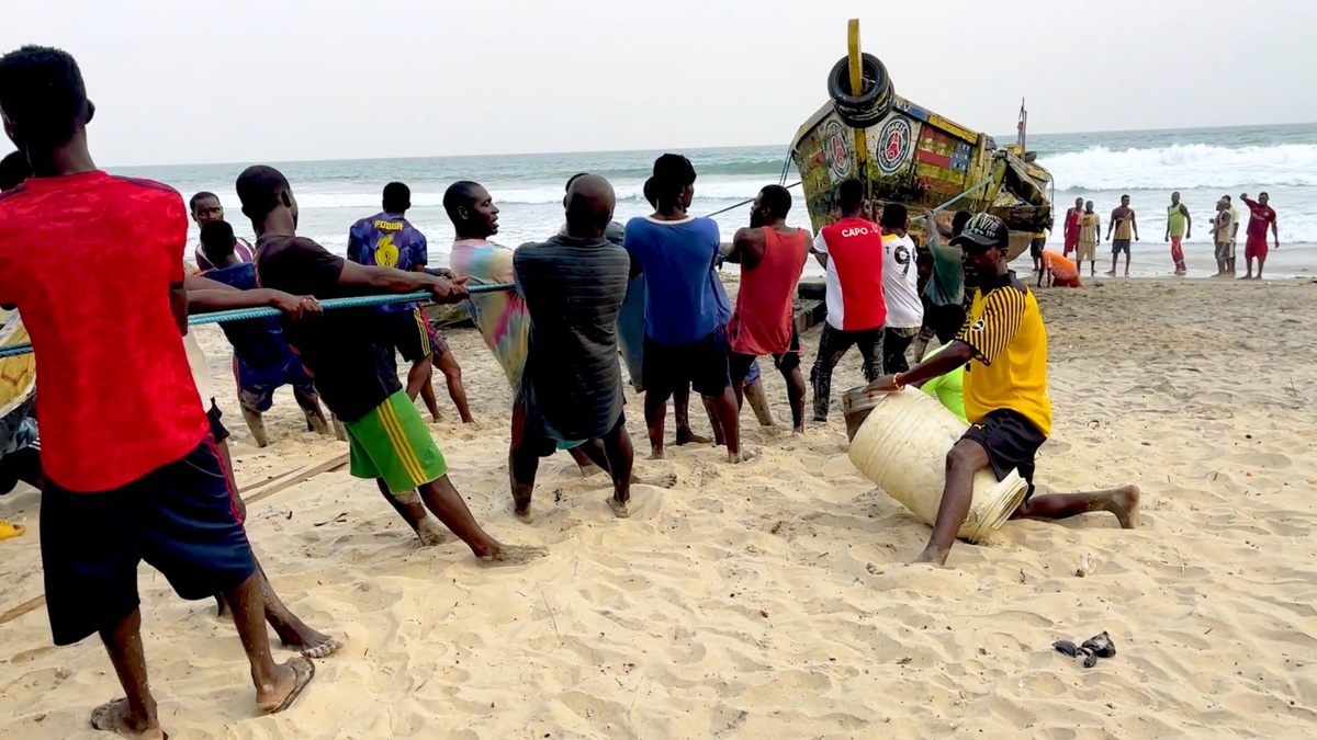 Small-scale fishers in Ghana are pulling a fishing vessel to a shore.