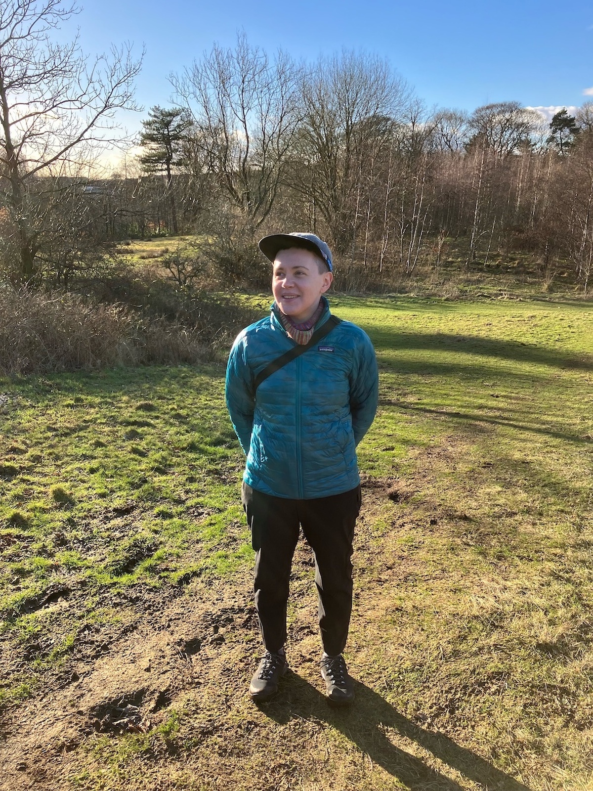 Emma Balkind standing in a sunny green space, wearing a blue jacket and cap.