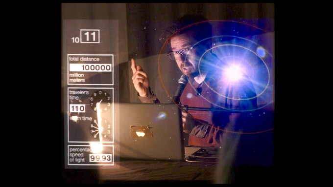A seated man speaking animatedly with index finger raised, superimposed over an image of the solar system.