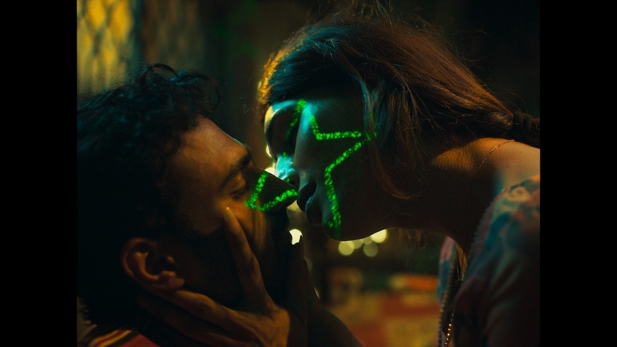 A man and a woman about to kiss, in a dark room. She gently holds his face, as a green star illuminates their faces.