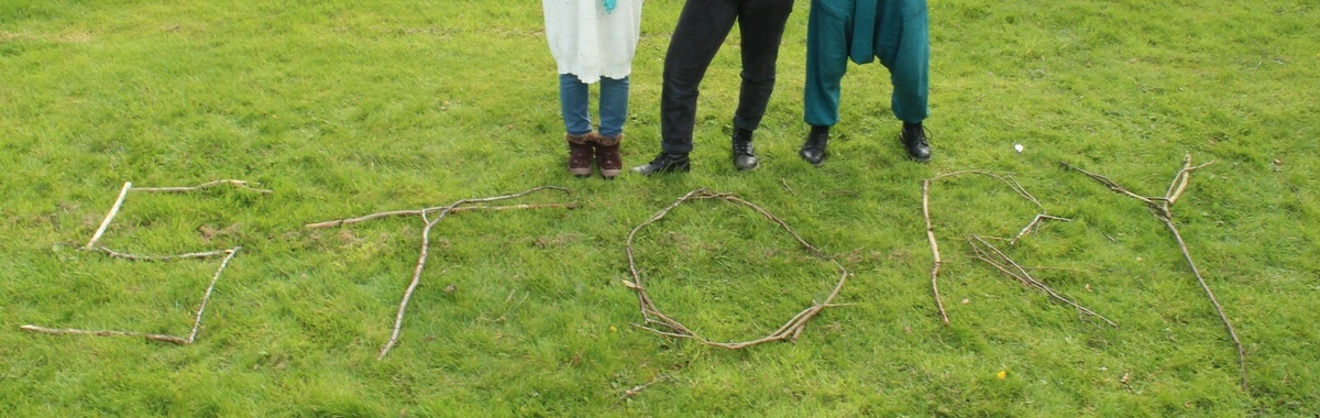 A field of grass with sticks that spell out the word "STORY", three people's legs are visible at the top of the frame.