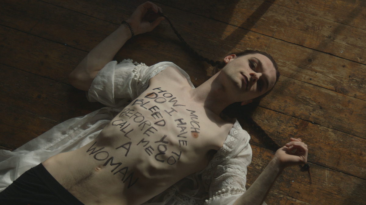 A woman lying on the floor her chest is bare with "How much do I have to bleed before you call me a woman" written on it