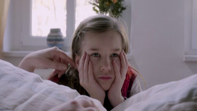 A child lies on the bed with their head in their hands.