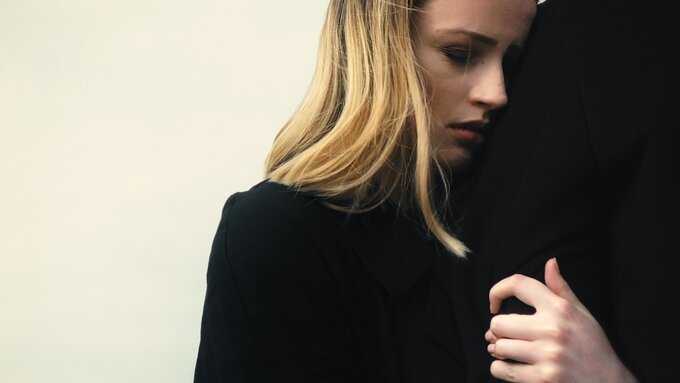 a young woman with blonde hair holds on tightly to the arm of the anonymous man next to her