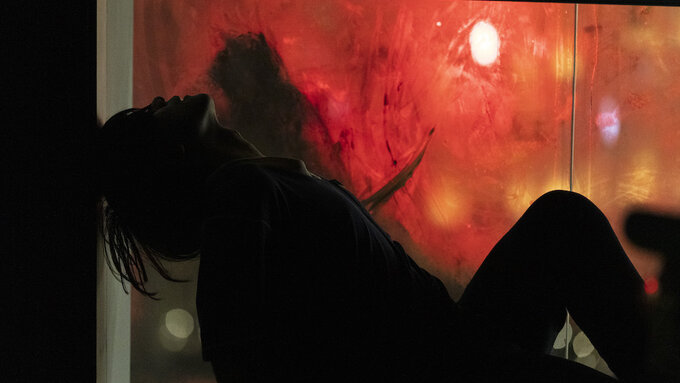 Silhouette of a person  laying against a window. The window is fogged up & reflects red lights from outside.