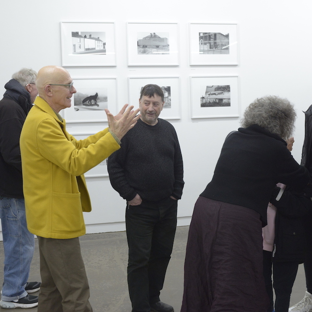 Francis McKee stands in the middle of a gallery, with many people around him.