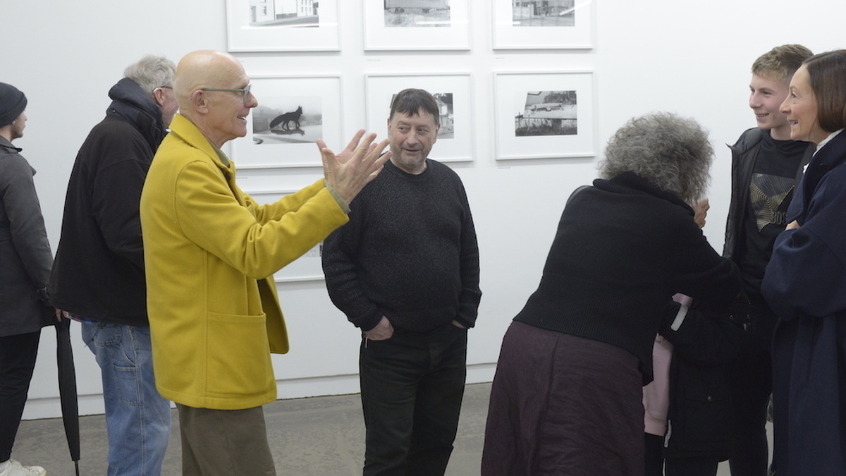 Francis McKee stands in the middle of a gallery, with many people around him.