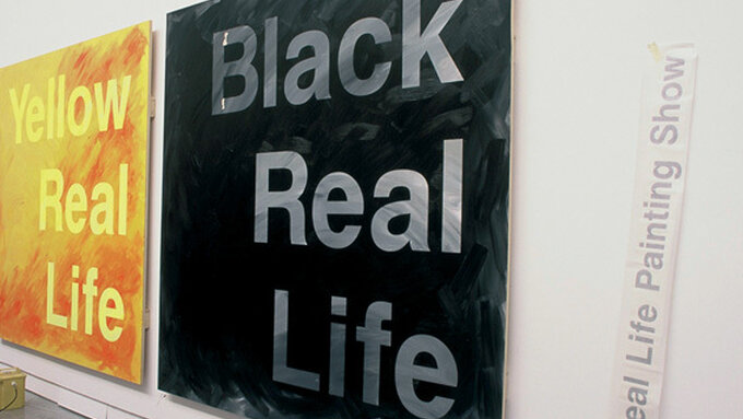 A photo of a painting installed in the CCA space, a black painting full of texture with text that reads Black Real Life