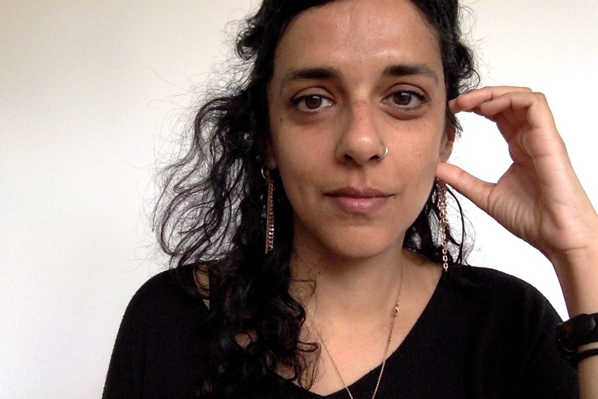 A photograph of Ayesha, a brown skinned femme person with long black hair, brown eyes, a nose ring, and long earrings.