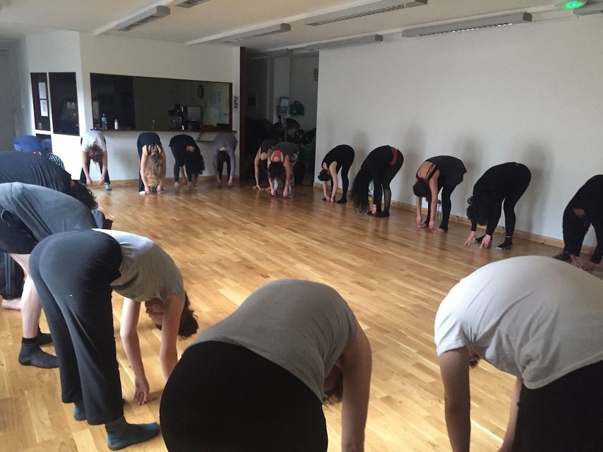 A group of dance participants warming up, bending over from the waist and releasing downwards towards the floor.