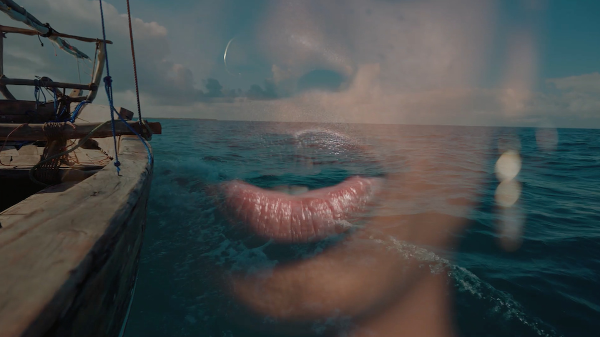 A Black African person’s mouth slightly open overlaid over the prow of wood over a turquoise ocean and blue sky.