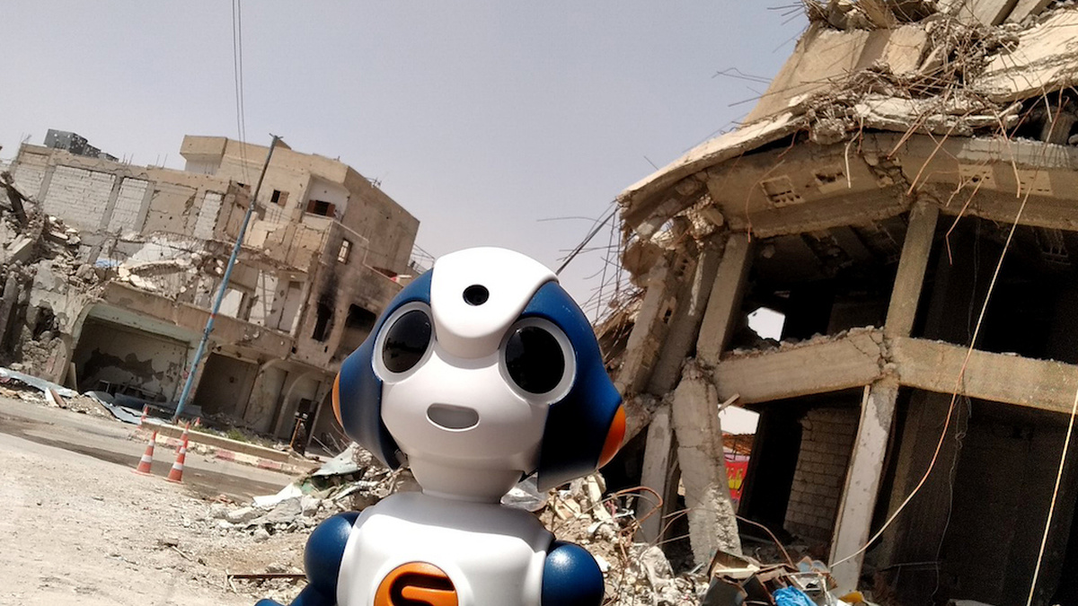 A bright plastic robot in the foreground with two devastated buildings, stripped down to their concrete shells.