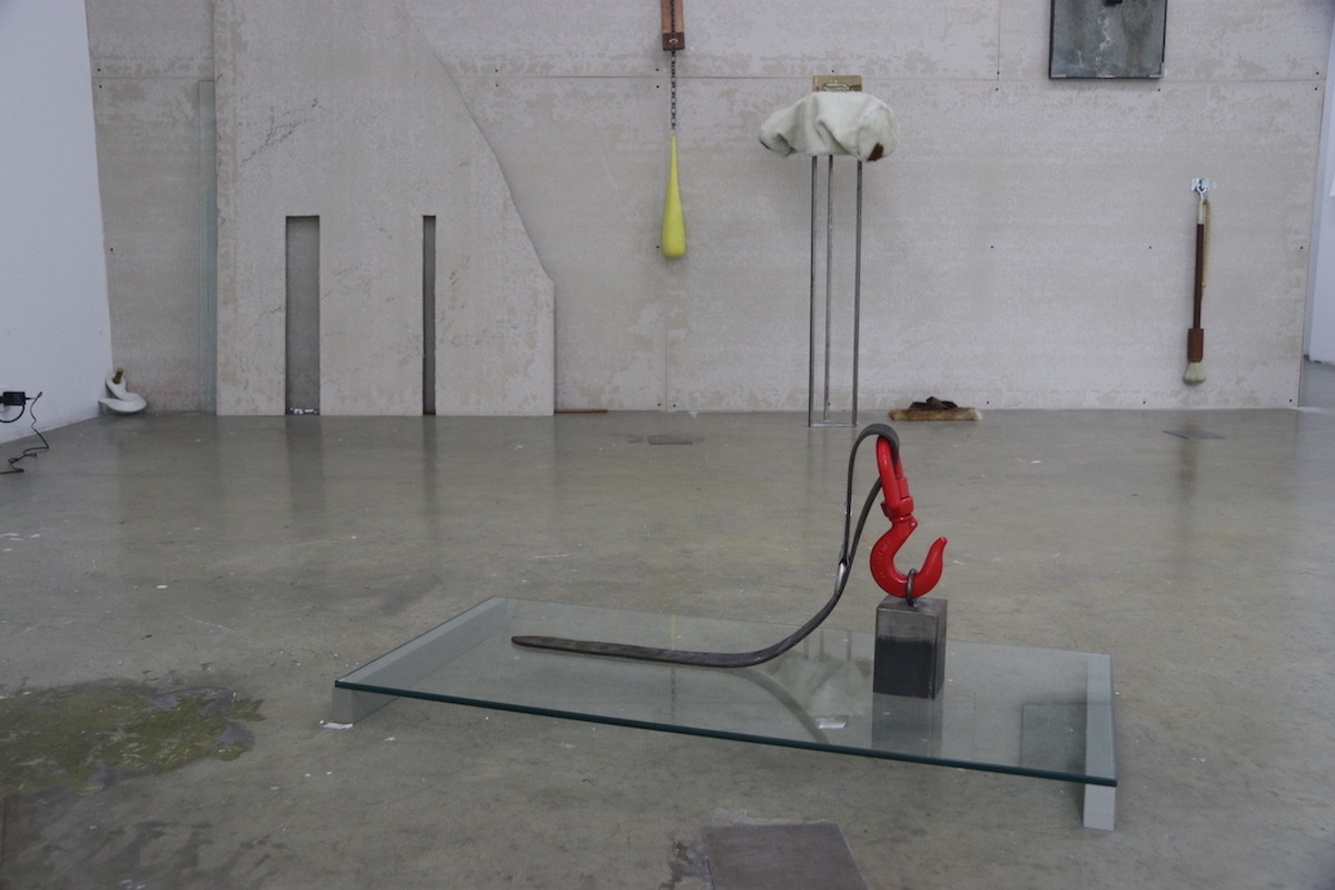 An industrial art space: a piece of glass, with a concrete block with a red metal hook with a black leather strap on it