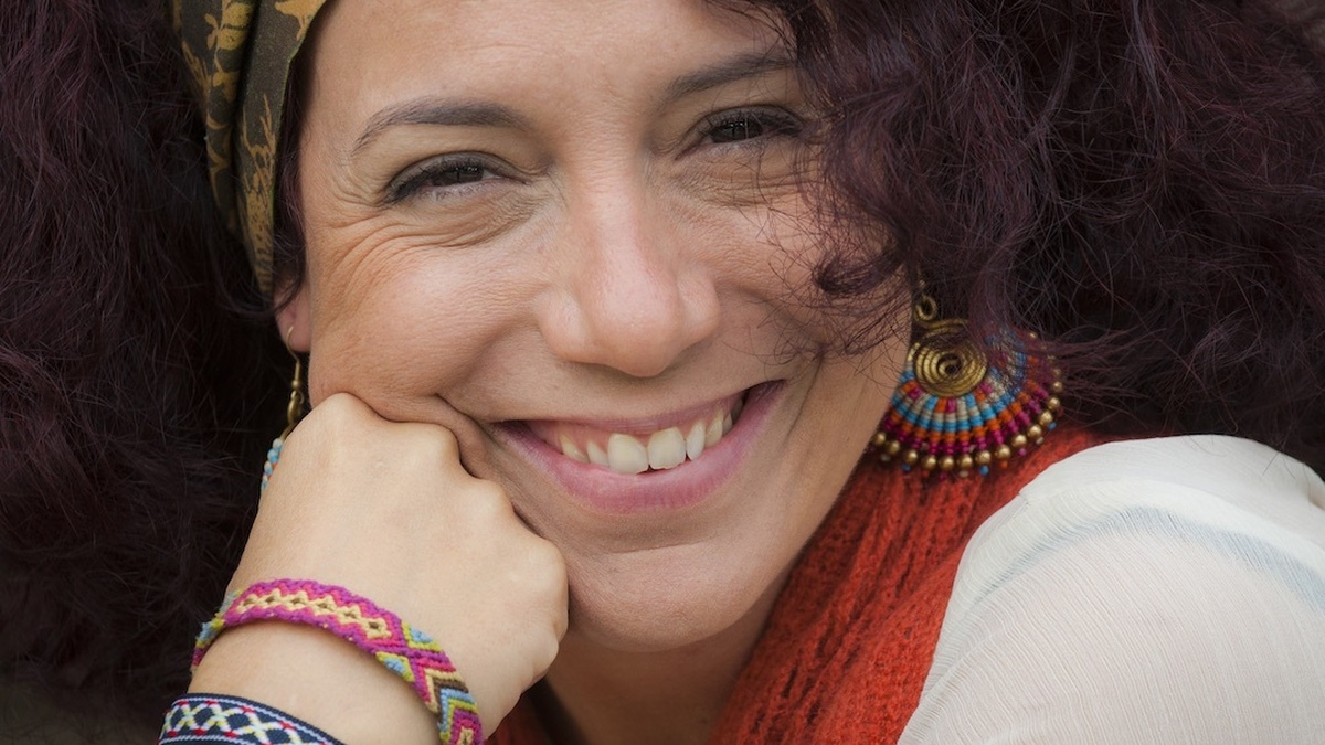A portrait of a woman who is smiling, wearing a green headband and orange scarf