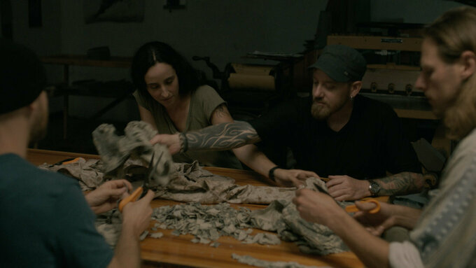 Four veterans, two men and two women sit at a table cutting up their military uniforms.