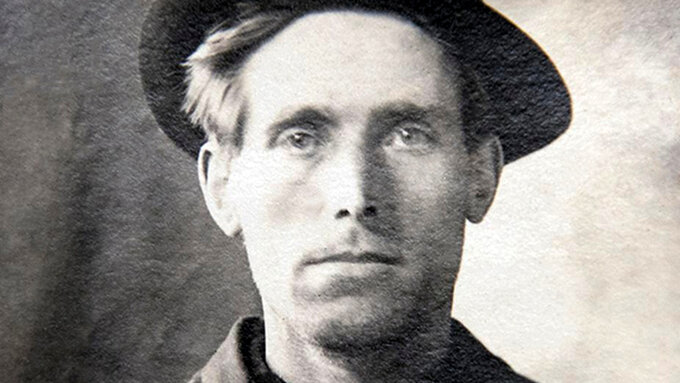 An old black and white photo of activist Joe Hill. A white man wearing a serious expression and a fedora.