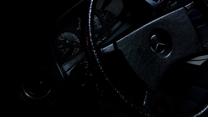A shot of the interior of a Mercedes limo. The scene is dark and the steering wheel reflects the glowing dials' light.