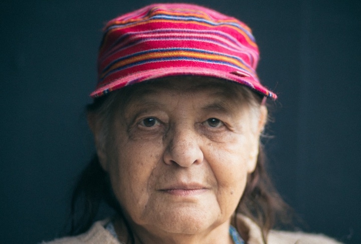 A photo of Marta Rodríguez, an older Latin-American woman with sharp brown eyes. Wearing a red columbian patterned cap.