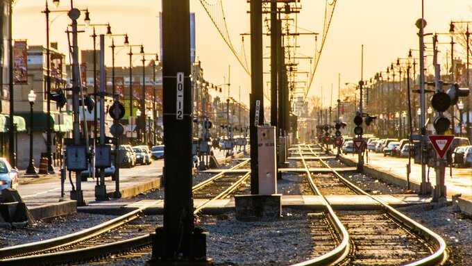 A photograph at dawn of a tramway running along the centre of an urban street. It is bathed with golden light.