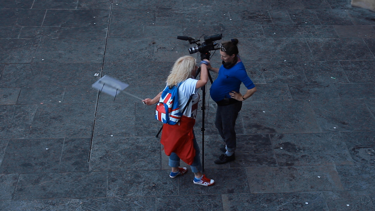 A pregnant film maker is being passionately spoken to by a woman wearing a union flag outfit.