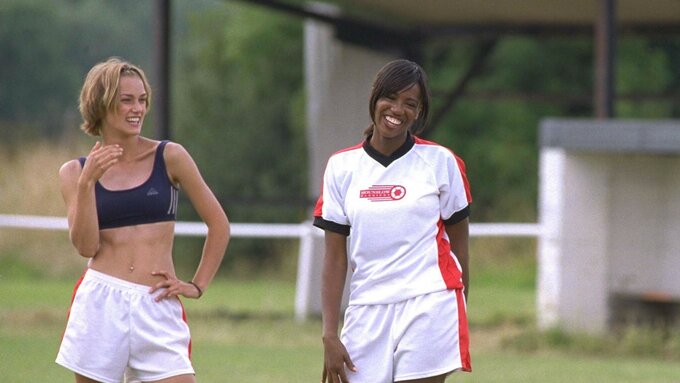Stil from Bend it Like Beckham featuring two women laughing and walking on a football pitch