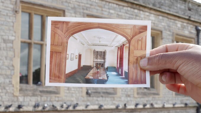 Image of a hand holding up a photo of a room with a long table with seats around it