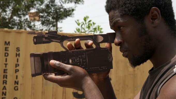 A black man holds a video camera.