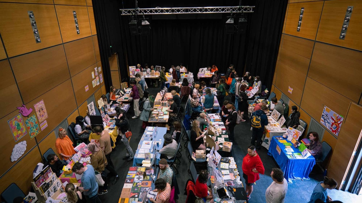 The zine fair from above. There are tables with people sat at them selling their zines. People are browsing the tables.