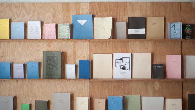 Three rows of colourful booklets in different sizes against a plywood wall.