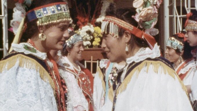 Two women in traditional dress facing each other smiling.