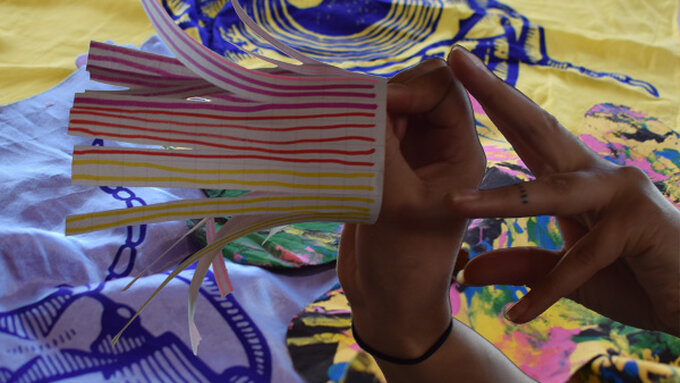 hands holding a small paper portal against a backdrop of brightly printed fabrics