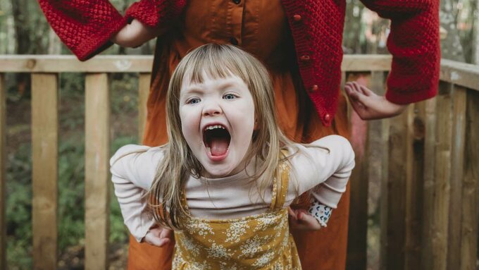 A mother and child outside with trees in the background. The child is laughing.
