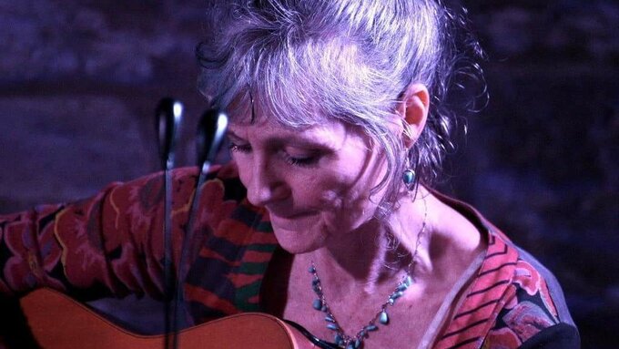 Woman with grey hair playing the guitar.
