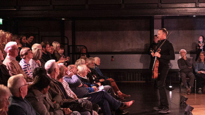 A man holding a violin stood in front of a watching crowd.