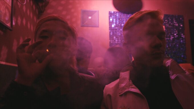 Two people sitting in a pink-lit club room.